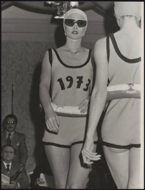 Fashion show with models wearing swimming caps and swimsuits embellished with '1973', and inflatable rubber rings round their waists