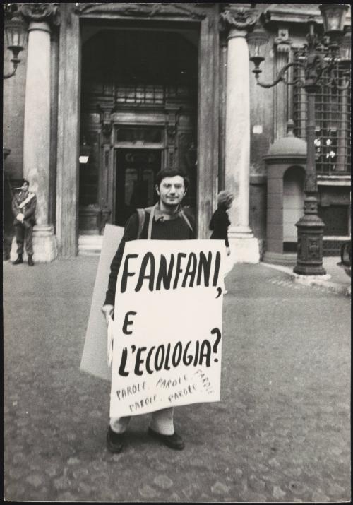 A man in a lonely demonstration wears a placard that reads:
'Fanfani e L'ecologia?'
