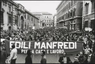 Construction workers demonstrating for contracts in Rome.
A large banner reads:
'Edili Manfredi per a casa e lavoro' 

'Manfredi constructions. For home and work.' 


