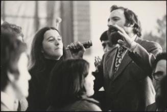 Anarchist demonstrators listen to a man speaking through a microphone