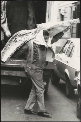 A man carries a frozen cow carcass from a van on market day