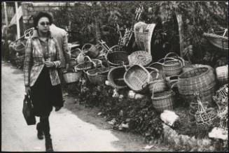 A womanwalks by wicker baskets for sale, lining the road on market day
