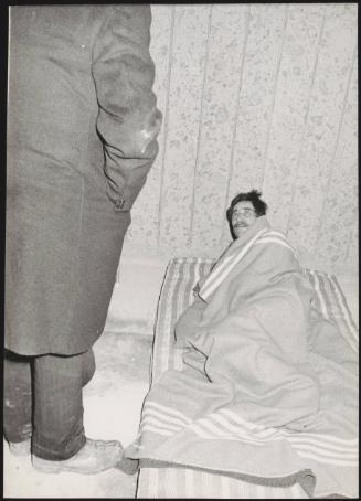 A refugee survivor rests on his makes shift bed. Another man in a large over coat stands over him during the aftermath of an earthquake in Tuscany that left about 5,000 homeless