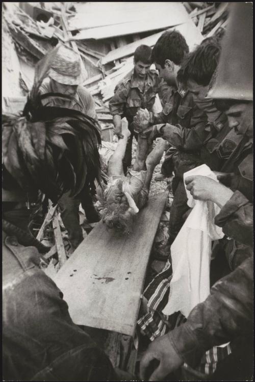The body of a victim of the Friuli earthquake is lifted on to a stretcher by police and soldiers