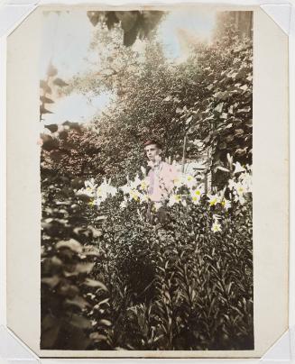 A young man wearing a pink shirt among lilies in a garden