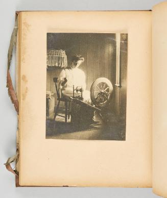 [A woman works at her wheel in soft daylight with intricate textile work on the wall.] [Page 57 of Quebec I; from collection of Canadian albums compiled by Edith S. Watson, 1890s-1930s]