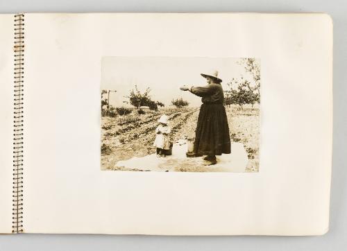 [Woman letting grain sift through her fingers, with child beneath her, page 19 of The Doukhobors I album]
