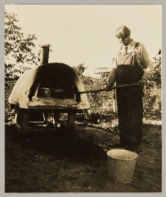 A "farmerette" of the Canadian prairie tendig the big loaves of bread a-baking in the out-of-door oven In Gonor, Man.
