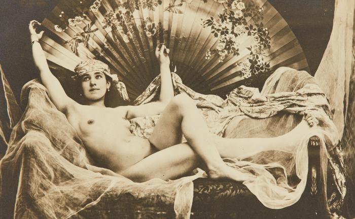 [Woman seated on bed with large decorated fan]