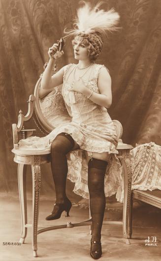 [Woman wearing feathered hat at dressing table]