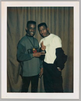 [Two young men making peace signs posing in front of brown curtain]
