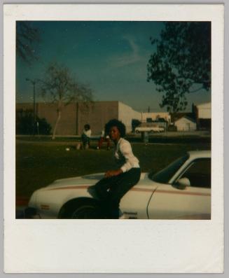 [Woman sitting sideways on hood of car]
