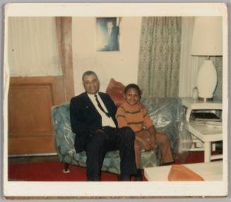 12-29-68 [Man in suit with arm around boy sitting on plastic wrapped couch]