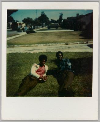 [Two men with afros laying on grass lawn]
