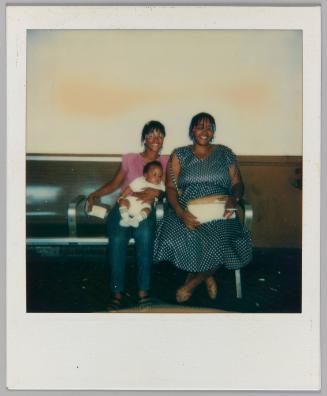 6-16-85 [Two women with beaded cornrows seated on bench with baby]
