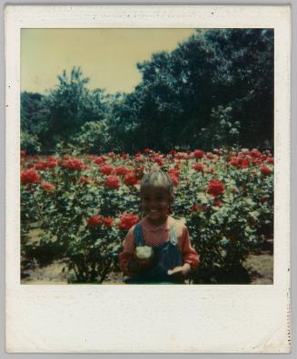 [Young girl eating apple in front of field of flowers]
