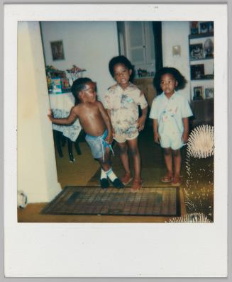 [Two boys and one girl in summertime outfits stand on metal grate]
