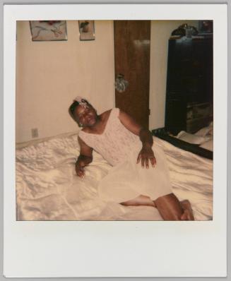 [Person in nightgown reclining on bed with their hand on their leg, door and dresser behind them]
