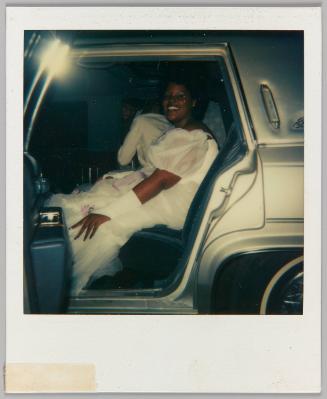 [Woman in wedding dress sitting in back seat of car]
