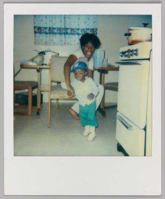 Greg 11 mos. [Girl holding hands with toddler in kitchen]
