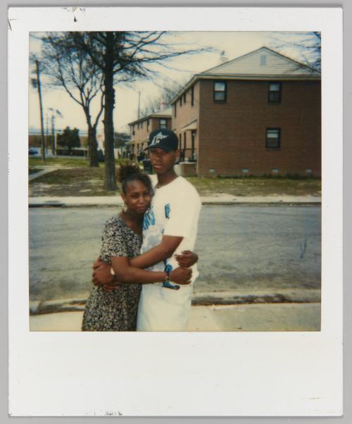 [Teen girl and teen boy embracing on the street outside of brick house]
