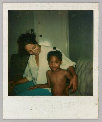 [Woman in white shirt smiling and embracing topless child]
