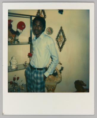 [Man with moustache posing indoors with knick knacks]