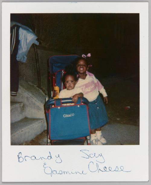 Brandy & Jasmine Say Cheese [Young girl in pink and white sweatshirt leaning on "Graco" brand stroller with toddler in it]