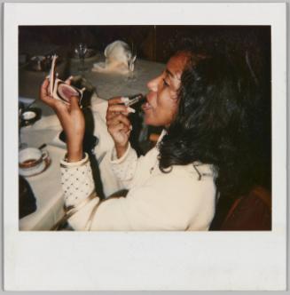 [Profile of woman holding a compact mirror and applying lipstick]