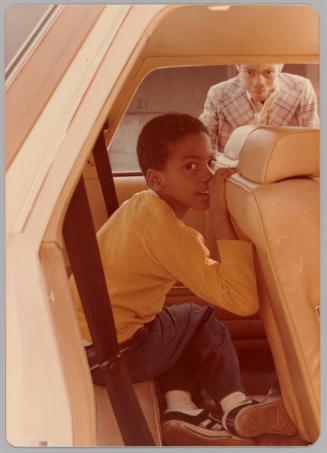 [Little boy in back seat of car, older boy staring through the car window]
