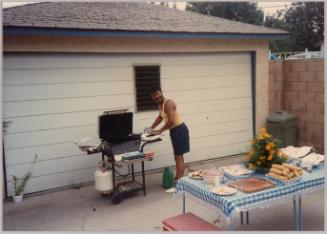 [Man at barbecue in front of garage] 
