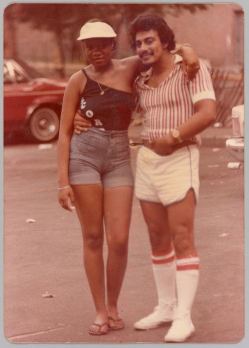 [Woman and man with arms around each other in parking lot, dressed in summer clothing, man wearing knee high socks]
