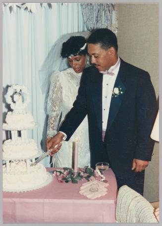 [Newly weds cut their wedding cake on pink table cloth] 
