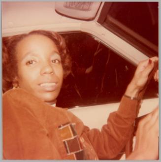 [Young woman in drivers seat of car with hands on steering wheel]
