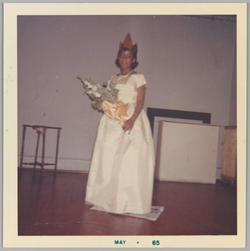 [Young woman posing in white dress, wearing gold crown and holding bouquet of flowers]
