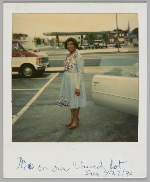 Me at our church lot Sun. 4/27/90 [Woman in a dress and red shoes standing by the open door of a parked car]
