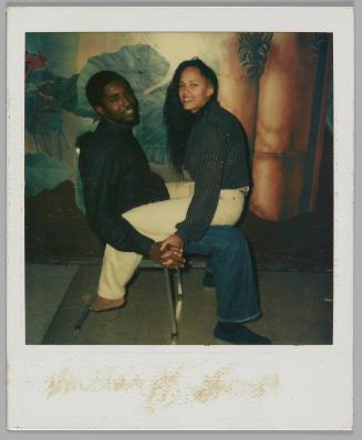 24 June 1983 [Man sitting on chair with woman in white pants sitting on his lap and facing him, they are holding hands and have their heads turned towards the camera]