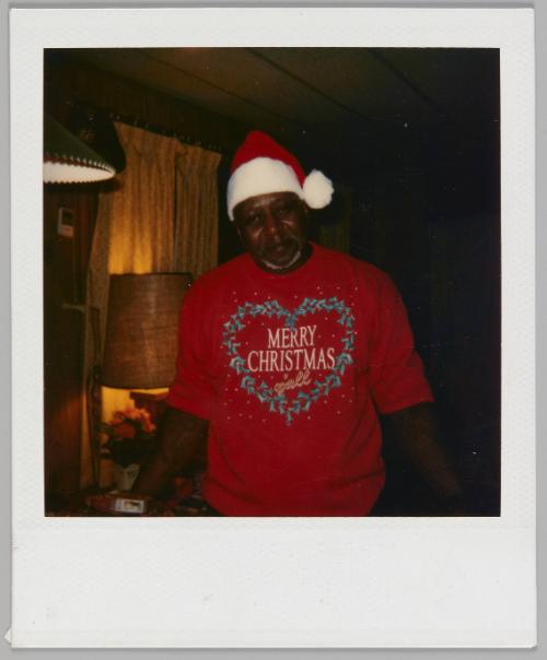 [Man in Santa Claus hat and red sweater with a heart-shaped wreath and the words "Merry Christmas y'all"]
