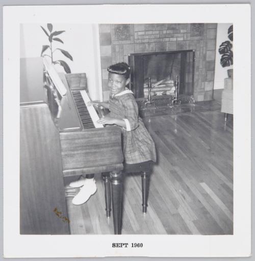 [Little girl in dress sitting on piano with her hands onthe keys]