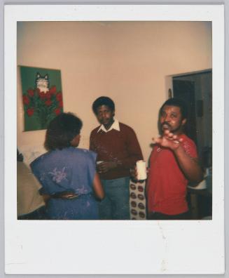 [Woman and two men conversing, man on right gestures hand to camera]