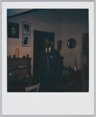 [Underexposed image of young man standing in living room area wearing a cardigan]
