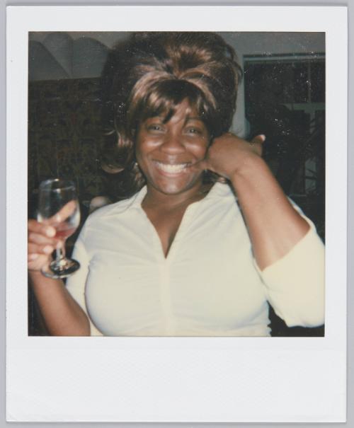 [Woman with big updo holding a wine glass in one hand and gesturing with the other]