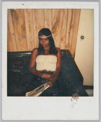 [Young woman sitting on brown leather couch wearing a braid headband]