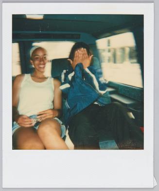 [Two adolescents in backseat of car, teen on right covering their face]