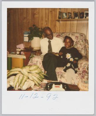 11-12-92 [Elderly man sharing seat with little girl in dress covered with daisies]