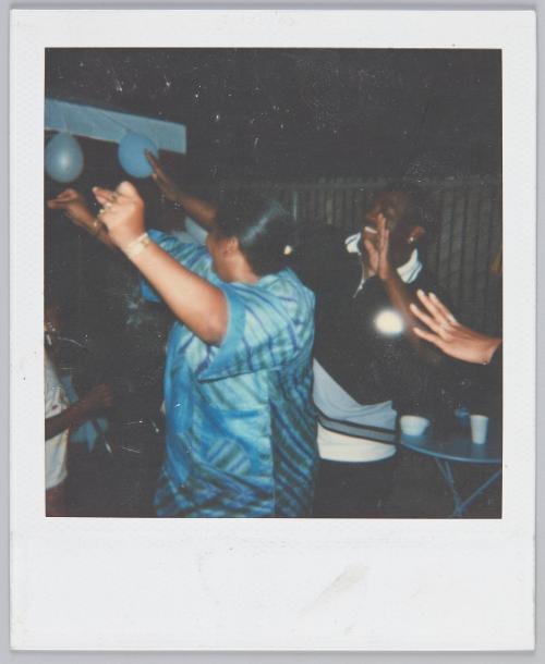 [People dancing with their arms in the air, woman in foreground wears silver blue top]