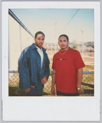 [Young man in red tshirt standing next to young man wearing oversized denim shirt]