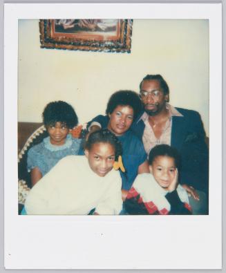 [Man and women sitting on couch surrounding by three kids]