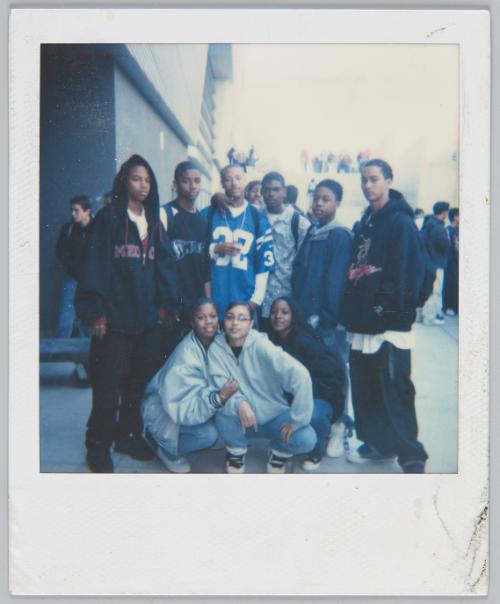 [Group of nine adolescents posing, young man in middle wears a blue football jersey]