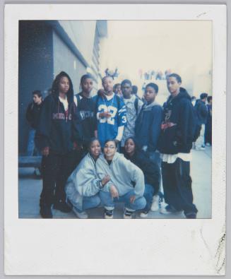[Group of nine adolescents posing, young man in middle wears a blue football jersey]